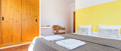 A bedroom with a bed, a wooden wardrobe, a chair, and a bedside table.
