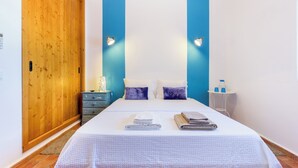 A bedroom with a wooden wardrobe, a bed with white bedding, two wall-mounted lights, and a small bedside table with a lamp. - Monte da Eirinha (Mertola)