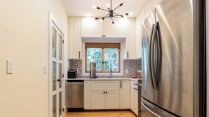 Una cocina moderna con un refrigerador de acero inoxidable, gabinetes blancos, un ventanal con vistas y una araña.