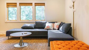 Una sala moderna con un sofá modular, una mesa de centro redonda y un ventanal con persianas.