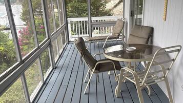 A covered outdoor area with a table and chairs, large windows, and a view of a body of water.