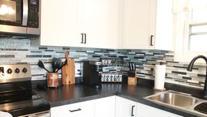 Una cocina moderna con armarios blancos, un lavamanos de acero inoxidable, una cafetera y un microondas.