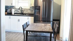Una cocina moderna con armarios blancos, un refrigerador de acero inoxidable, una mesa de comedor de madera y un ventilador de techo.