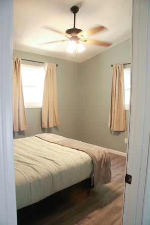A bedroom with a bed, a ceiling fan, and curtains.