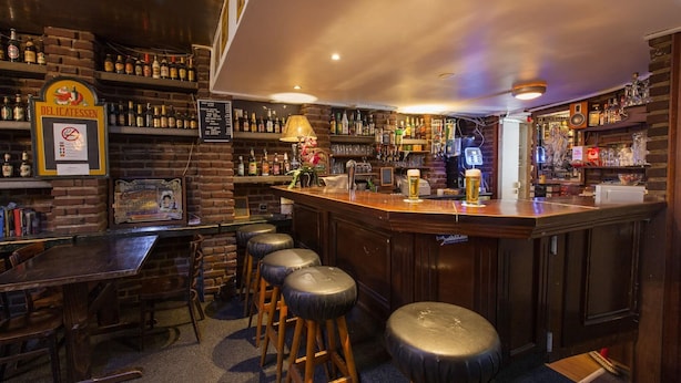 A bar area with stools, a bar counter, and shelves of liquor bottles. - Travel (Amsterdam)
