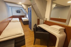 A compact room with two single beds, a small desk with a chair, and a television on the wall. - Travel (Amsterdam)