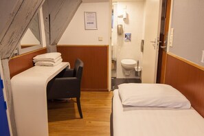 A compact hotel room with a bunk bed, a desk with a chair, a small bathroom with a toilet and sink, and a wooden ceiling. - Travel (Amsterdam)