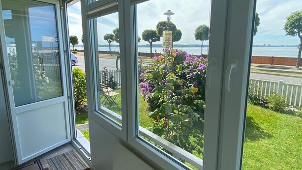 Una habitación con amplios ventanales que dan a un jardín y a un cuerpo de agua.