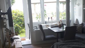 Un dormitorio con cama, escritorio y silla. Se ve vegetación por la ventana.