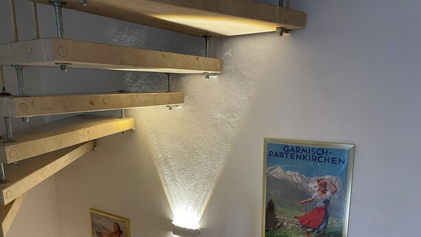 A room with a wooden ceiling structure, a wall-mounted light fixture, and two posters.