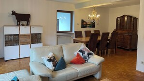 A living room with a sofa, a dining table with chairs, a chandelier, and a cabinet.