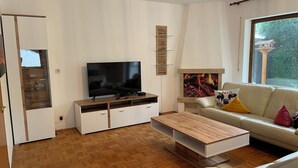 A modern living room with a flat-screen TV, wooden coffee table, white sofa, and a fireplace.