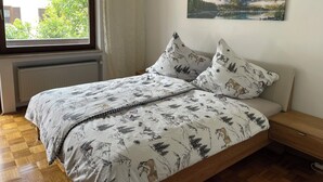 A bedroom with a bed, a window, a radiator, a wooden floor, and a painting on the wall.