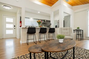 A modern kitchen with a central island, black bar stools, a round coffee table with a plant, and a leopard print rug.