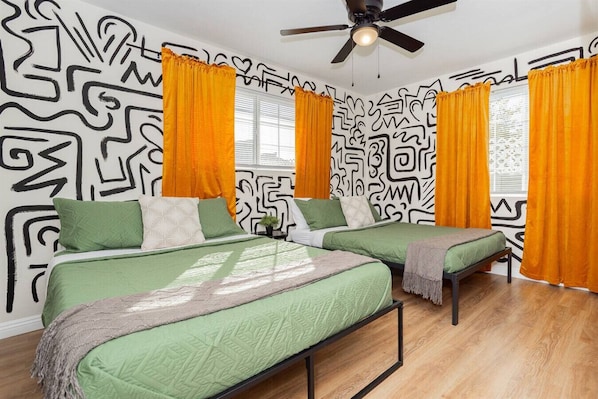 A room with two beds, a ceiling fan, and patterned walls.