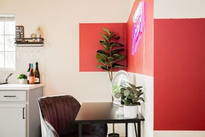 Une pièce comprenant une table à manger, une chaise, une plante en pot, un miroir et une étagère avec des bouteilles et une enseigne.
