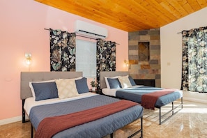 A bedroom with two beds, a stone fireplace, and an air conditioning unit.