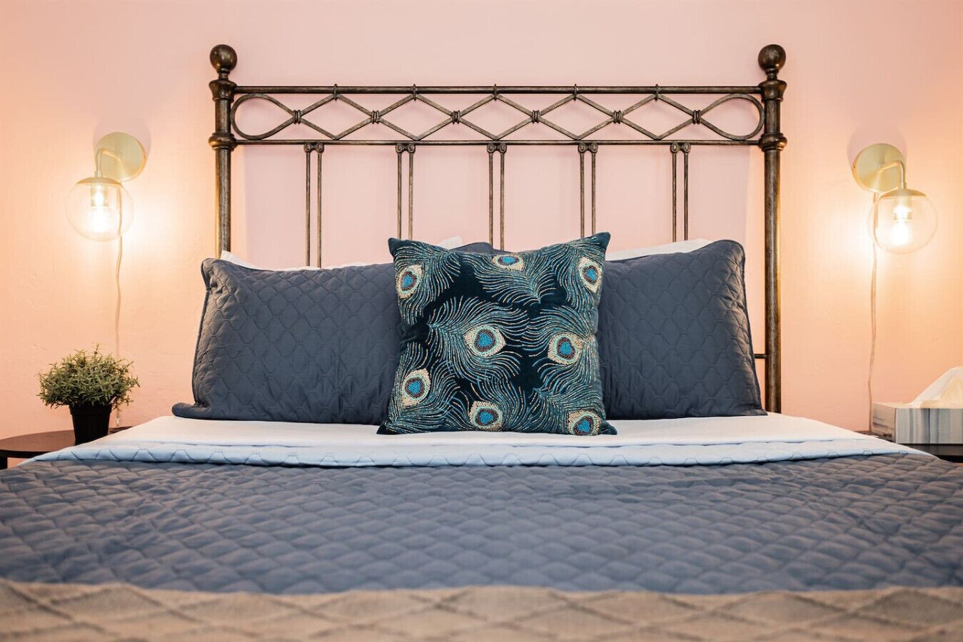 A bed with a metal headboard, two wall-mounted lamps, and a small potted plant.