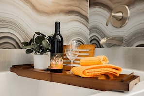 A bathroom with a marble wall, a bottle of wine, a glass, a towel, and a plant.