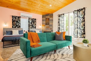 A modern living room with a teal sofa, a bed with a grey headboard, and a stone fireplace.