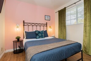 A bedroom with a bed, two bedside lamps, a picture on the wall, and a window with curtains.
