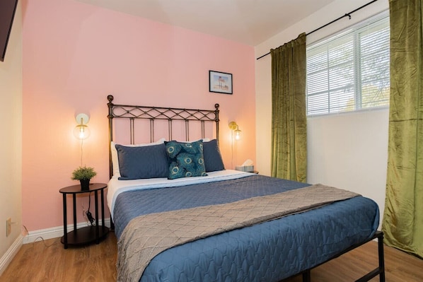 A bedroom with a bed, two bedside lamps, a picture on the wall, and a window with curtains.