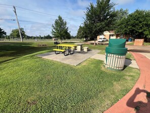 A picnic area with tables and benches, a trash can, and a paved walkway. - Cozy Home Wt Hot Tub, WiFi n Smart Tv (Midwest City)