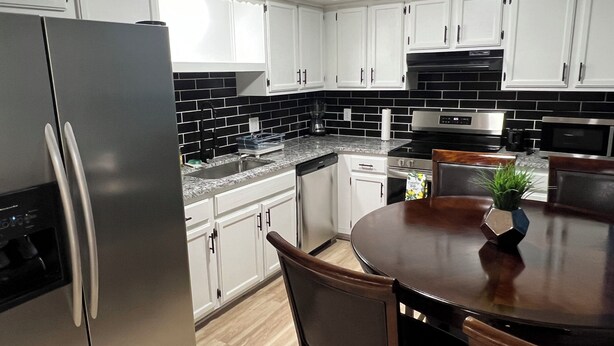 Cocina moderna con armarios blancos, un refrigerador de acero inoxidable, salpicadero de baldosas negras y una mesa de comedor de madera.