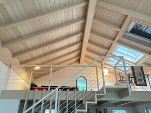A high-ceilinged room with a wooden ceiling and skylight, a white staircase, and a view of the outdoors through a window. - the silence among the olive trees, on a hill overlooking the sea (Imperia)