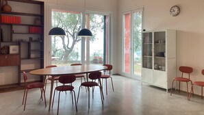 Un'ampia stanza con un grande tavolo da pranzo circondato da sedie, soffitto in legno e un'ampia finestra vista alberi.