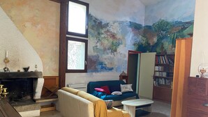 Un salon comprenant un canapé, une table basse, une cheminée, une bibliothèque et une fresque murale.