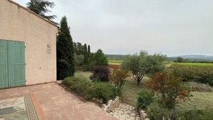 Un espace extérieur aménagé avec un revêtement pavé, un mur en pierre, une porte verte et une vue sur un paysage rural avec des champs et des arbres.