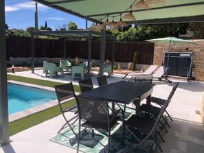 Relax by the pool under a covered patio with comfortable seating and a dining table.