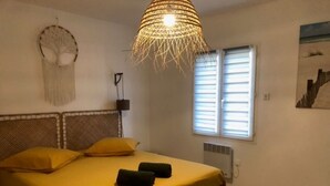 A bedroom with a bed, two pillows, a hanging light fixture, a wall-mounted artwork, and a window with blinds. - Villa Mapokia 2 Climatisée Avec Piscine Chauffée Privative Proche Uzès (st marcel de careiret)