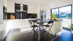 Une cuisine moderne avec des meubles blancs, un îlot central doté de sièges et une grande fenêtre offrant une vue sur l’extérieur.