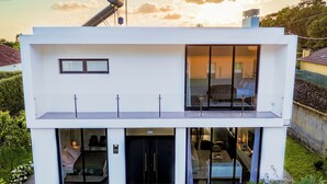 Une maison moderne à deux étages, dotée d’un balcon, de grandes fenêtres et d’un jardin bien entretenu.