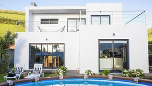 Une maison moderne à deux étages, dotée d’une piscine, de grandes fenêtres et d’un espace salon extérieur.