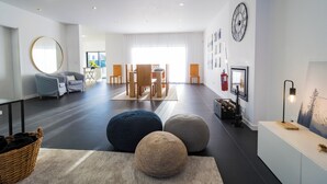 Un salon moderne avec un grand miroir rond, un coin repas avec une table et des chaises en bois, et une cheminée agrémentée d’une horloge murale.