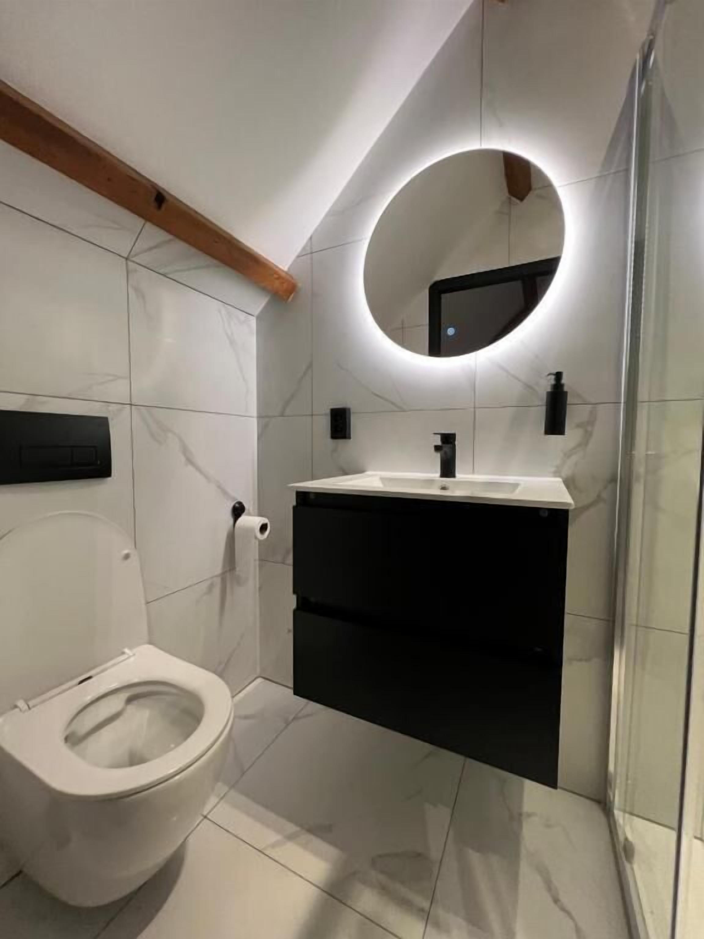 Une salle de bain moderne comprenant des toilettes, un meuble-lavabo avec un miroir et un espace douche.