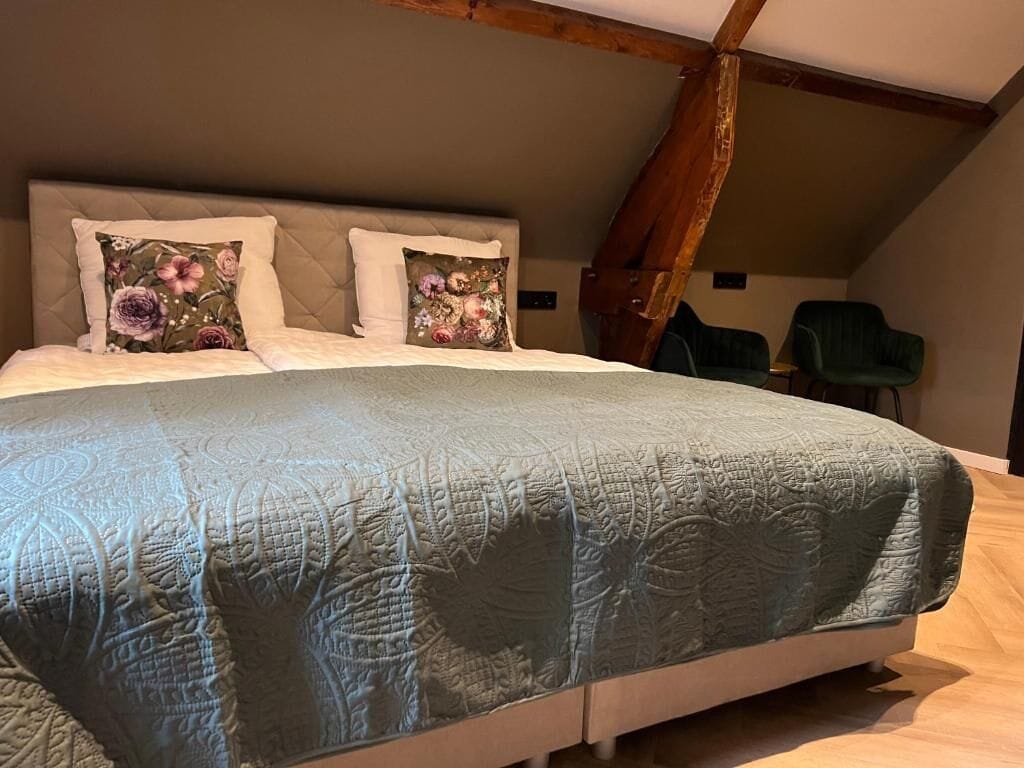 A bedroom with a large bed, two pillows with floral designs, a green quilt, and a wooden ceiling beam.