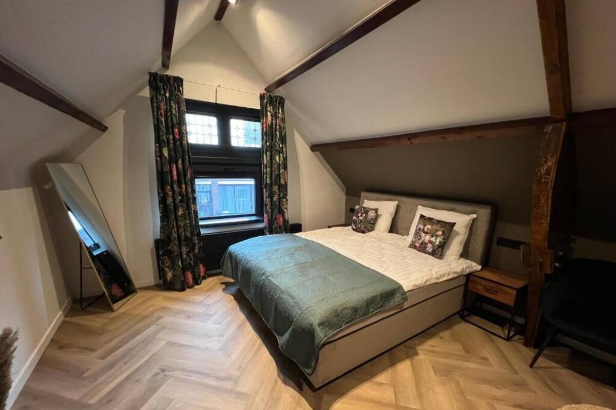 Une chambre à coucher avec un lit, une fenêtre avec des rideaux, un plancher en bois et un plafond en pente.