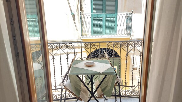 Ein Balkon mit Tisch und Stühlen, eine Schale auf dem Tisch und Blick auf ein Gebäude mit grünen Fensterläden.