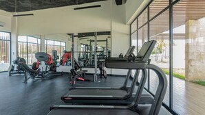 A modern gym with treadmills, weight machines, and a large window offering a view of the outdoors.