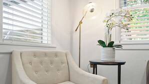 Una camera d'angolo con una poltrona beige, un tavolino con un'orchidea in vaso e una lampada da terra.