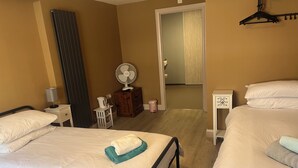 A hotel room with two beds, a wooden dresser, a fan, and a mirror. - Tumbledown Hotel (Shrewsbury)