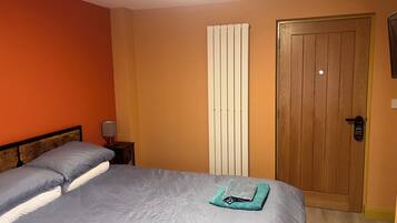 Un dormitorio con cama, mesita de noche, lámpara, radiador y puerta de madera.