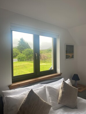 A bedroom with a large window, a bed with white linens, and a small bedside table with a lamp. - Cleadail Guest House (Skeabost)