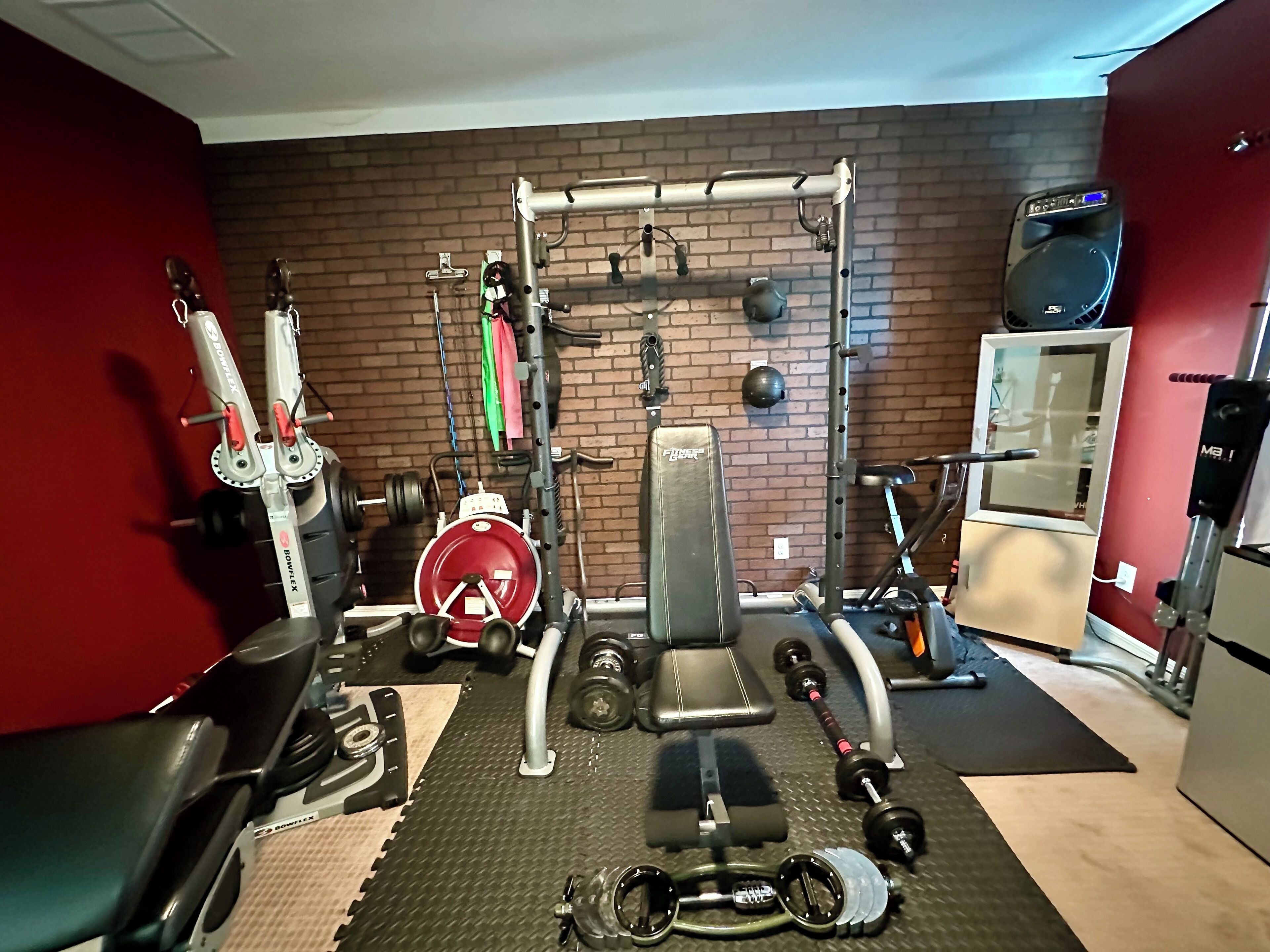 Un gimnasio en casa con una estructura para sentadillas, banco de pesas, mancuernas y discos de pesas.