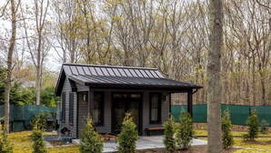 Eine kleine Holzhütte mit Veranda, umgeben von Bäumen und einem eingezäunten Bereich.