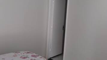 Una habitación con una cama cubierta por una colcha estampada, una puerta blanca y suelo de baldosas.